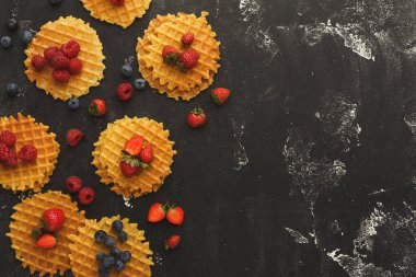 Koyu bir yüzeye çilek, ahududu ve yabanmersini serpiştirilmiş waffle 'lar konur. Düzenleme meyvelerin renklerini vurgulayan yaratıcı bir tasarım gösteriyor.