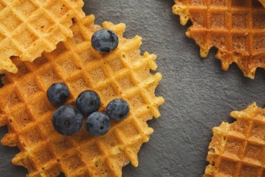 Yuvarlak bir waffle koleksiyonu gri bir yüzeye yerleştirilir. Taze yaban mersinleri bazı waffle 'ların üzerine saçılmış. Bu ayar basit bir kahvaltı sahnesini gösteriyor..