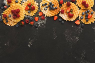 Koyu bir yüzeye yerleştirilmiş waffle 'lar çilek, yabanmersini ve ahududularla süslenir. Bu sette lezzetli bir tatlı için çeşitli renkli meyve sosları sunuluyor..