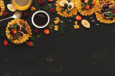 Bir waffle koleksiyonu, üzerinde çeşitli meyve ve şurup bulunan karanlık bir masada oturur. Etrafa saçılmış çilek, yabanmersini ve muzlar var. Bazı waffle 'lar kesilir ve şurupla gösterilir..