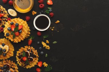 Bir waffle koleksiyonu karanlık bir yüzeye oturur. Taze böğürtlen, şurup ve muz dilimleri waffle 'ların etrafına dizilir. Yemek sunumuna odaklanmış kahvaltı zamanı..