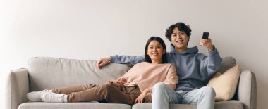 Bir erkek ve bir kadın televizyon izlerken bir kanepede rahatlar. Oturma odasındalar. Çift gülümseme ve rahatlıkla birlikte eğleniyor..