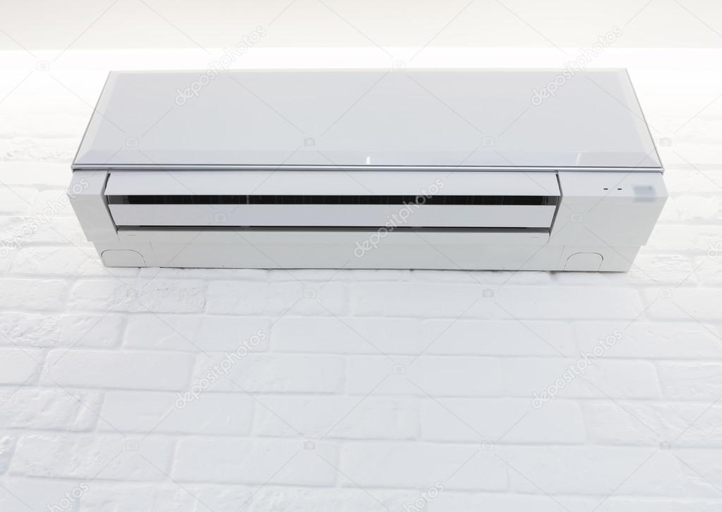 White air conditioner mounted on the brick painted wall