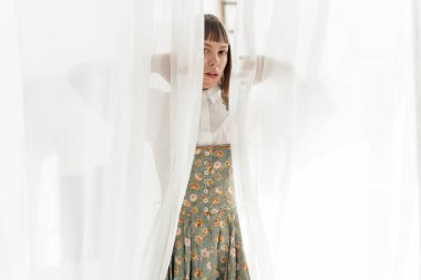 Pencerenin yanında poz veren eski moda elbiseli genç kız. 