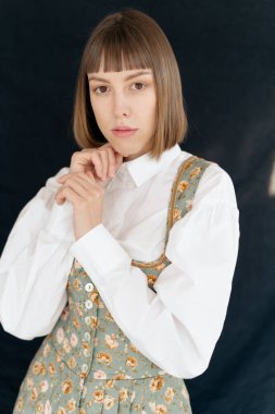 Eski moda elbiseli genç bir kadın stüdyoda karanlık arka planda poz veriyor.