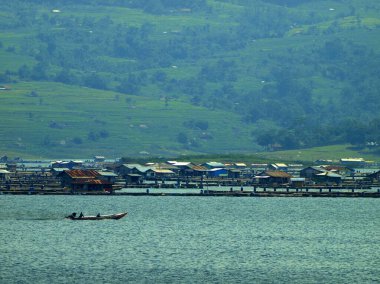 Geleneksel tekneler sakin göl suyunun üzerinden dağlık bir arka planla geçerler