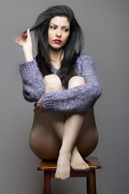 Çekici kız, uzun siyah saçlı kadın dışkı ve düşünme, gri bir arka plan üzerinde oturan.