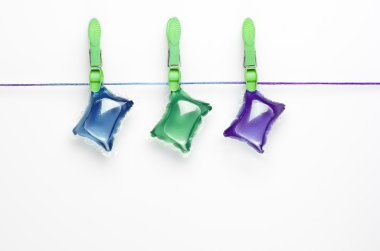 Colorful gel laundry capsules  hanging on washing line on white background.