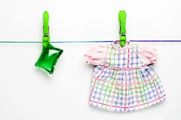 Зеленый гель капсулы для стирки и платье висит на стиральной линии на белом фоне . — стоковое фото