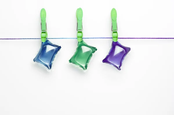 Colorful gel laundry capsules  hanging on washing line on white background.