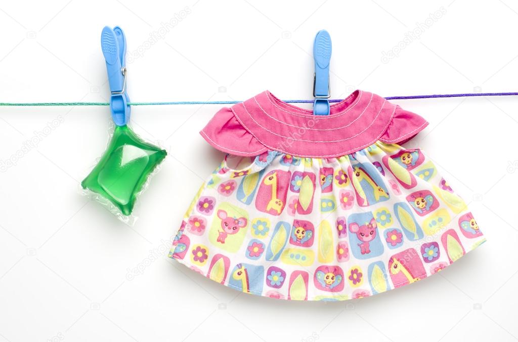 Green laundry gel capsules and dress hanging on washing line on white background.
