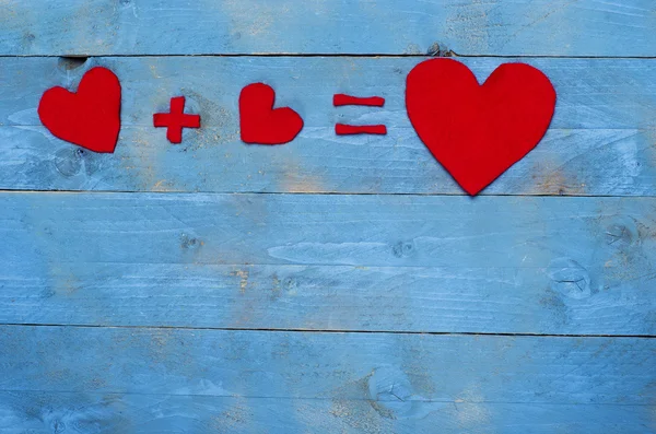 Equation with hearts arranged on blue wooden background. — Stock Photo, Image