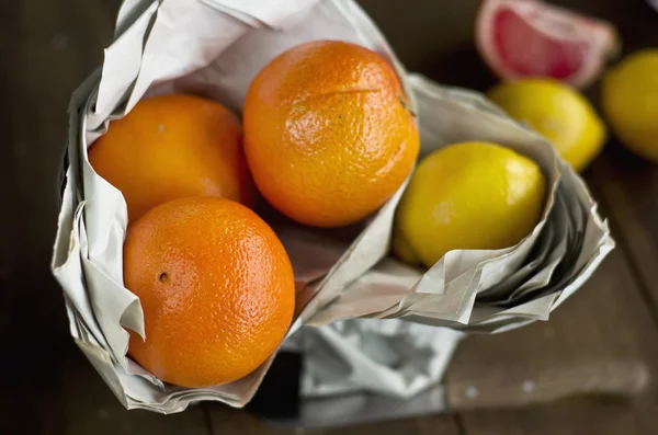 Naranjas, limones en papel sobre fondo de madera — Foto de Stock