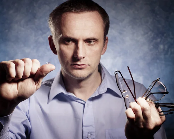 Man is comparing contact lens with glasses — Stock Photo, Image