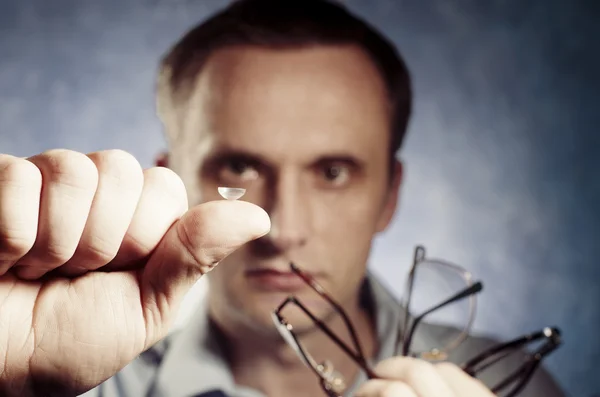 Man is comparing contact lens with glasses — Stock Photo, Image