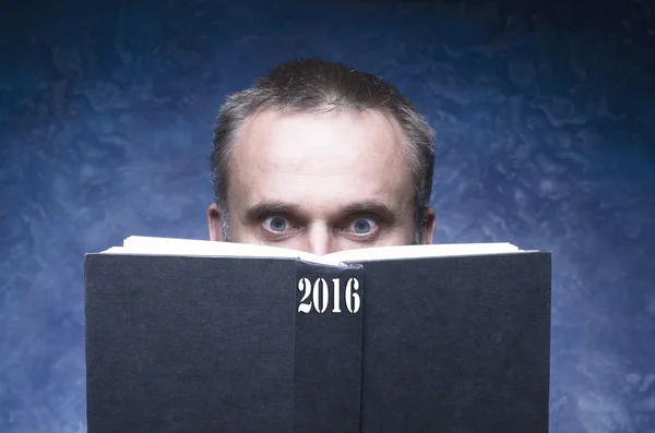 Hombre maduro siendo enfocado y enganchado por el libro, leyendo libro abierto, joven sorprendido, ojos increíbles mirando tapa en blanco, 2016 escrito en la columna vertebral del libro —  Fotos de Stock