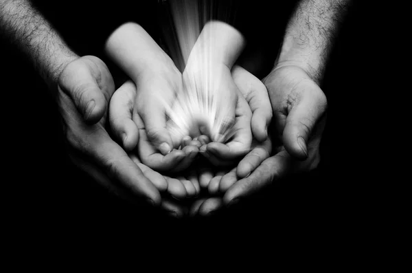 Spark of hope in a child hands who holding by parents hands on dark background. The light of faith.