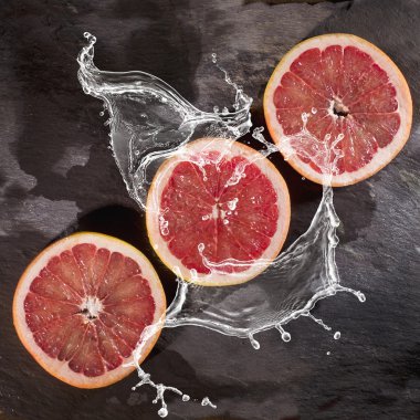 Üç siyah taş zemin üzerine suda sıçrayan greyfurt dilim.