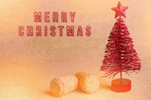 Feliz Navidad escrita con un pincel rojo brillante. Árbol de Navidad artificial rojo con corcho de champán sobre fondo brillante . — Foto de Stock