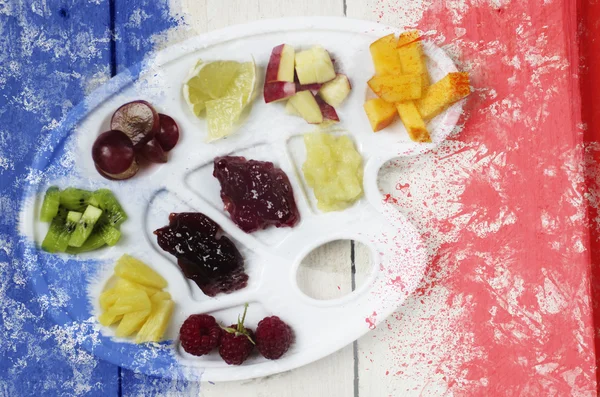 Bandera francesa creada a partir de colores salpicados azul blanco rojo sobre una pila de rodajas de frutas sobre una paleta de arte plástico blanco, fondo de madera . — Foto de Stock