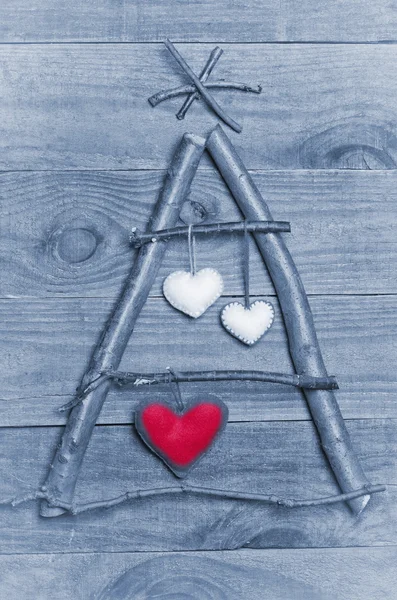 Christmas tree arranged from sticks, twigs, driftwood on wooden background.  Handmade hearts made from felt hanging on tree. Craft. — Stock Photo, Image