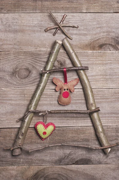 Christmas tree arranged from sticks, twigs, driftwood on wooden background. Handmade red and green heart, reindeer made from felt hanging on tree. Craft. — Stock Photo, Image