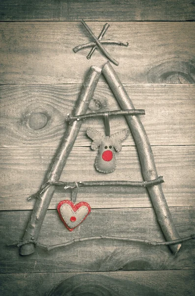 Christmas tree arranged from sticks, twigs, driftwood on wooden background. Handmade red and green heart and reindeer made from felt hanging on tree. Craft. — Stock Photo, Image