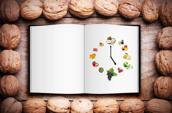 Einfacher Rahmen aus Walnüssen auf hölzernem Hintergrund. aufgeschlagenes Buch mit Bild der Uhr aus gesunden Früchten arrangiert. gesundes Lebenskonzept, Kopierraum. — Stockfoto