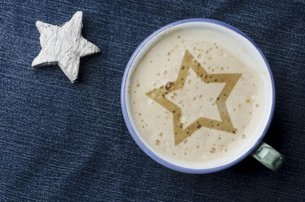 Tazza di caffè cappuccino con schiuma sotto forma di stella su jeans blu, sfondo denim. Stella di legno bianca . — Foto Stock