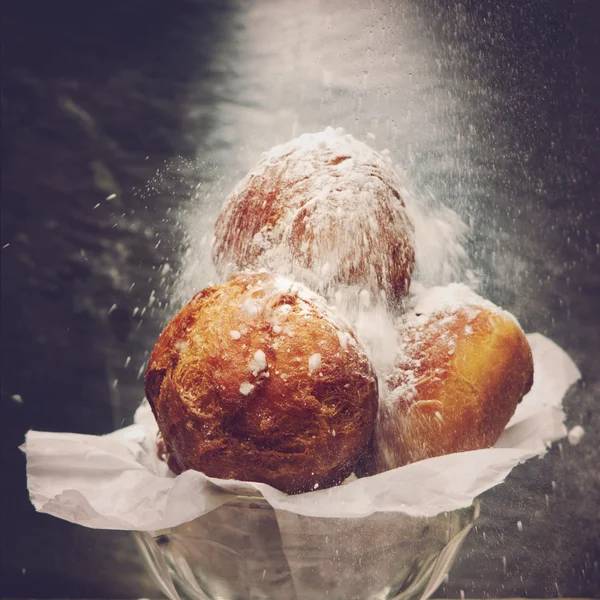 Rosquillas caseras, también conocidas como agujeros de rosquilla en un pedazo de papel de hornear en un tazón de vidrio, espolvoreado con azúcar en polvo . — Foto de Stock