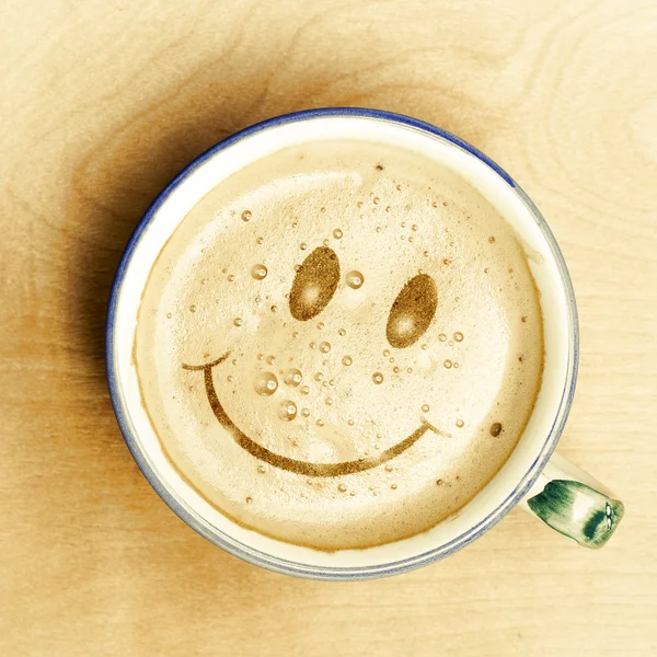 Gülümsemek yüz Cappuccino kahve fincan ahşap masa üzerinde köpük şeklinde