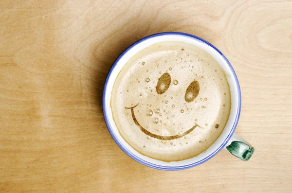 Schaumform des Lächelns Gesicht in Tasse Cappuccino Kaffee auf Holztisch — Stockfoto