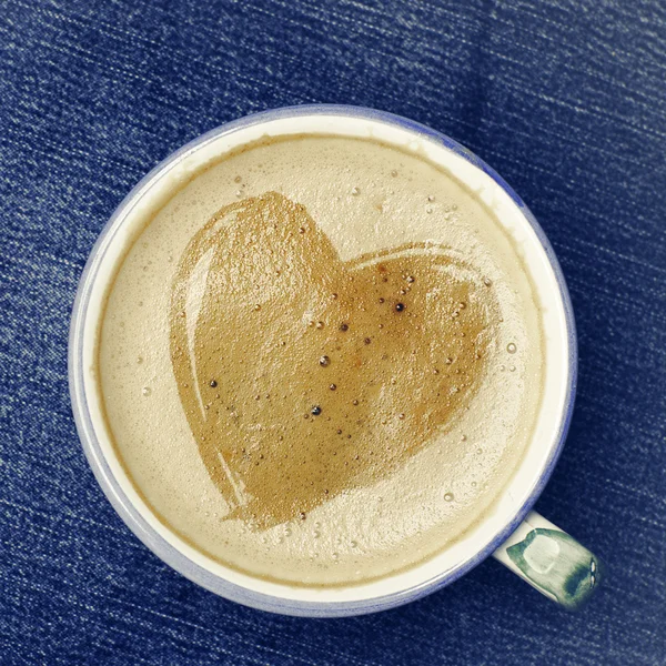 Tasse Cappuccino-Kaffee mit Schaum in Herzform auf Blue Jeans, Jeanshintergrund. rotes Herz handgefertigt aus Filz, Valentinstag-Konzept. — Stockfoto