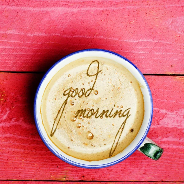 Una taza de café con leche, capuchino sobre una mesa de madera rosa. Palabras buenos días escritas en un café . —  Fotos de Stock