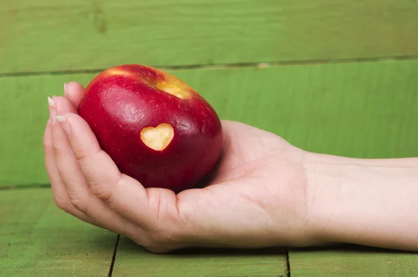 Maçã vermelha fresca com um corte em forma de coração na mão da mulher na mesa de madeira. Organismos geneticamente modificados isentos de OGM . — Fotografia de Stock