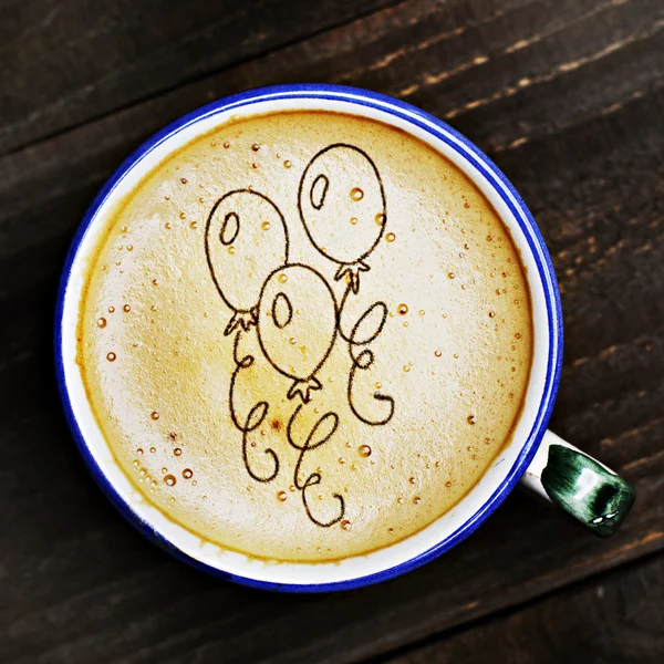 Cup of cappuccino coffee on wooden table. Balloons formed from coffee foam. Party time.