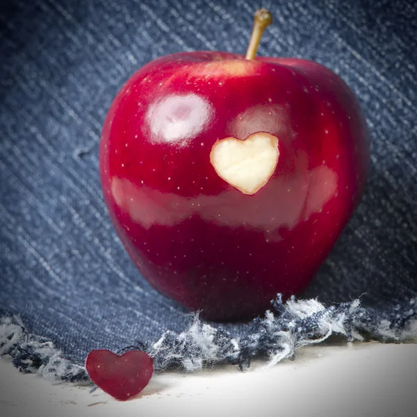 Rött äpple med en hjärtformade utstansade på jeans bakgrund. GMO-fria modifierade genetiskt organismer. Mors dag. — Stockfoto