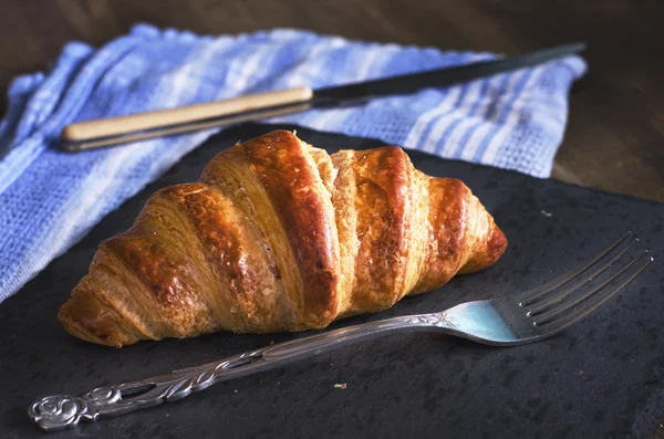 Croissant recém-assado em pedra preta. Toalha de cozinha azul no fundo . — Fotografia de Stock
