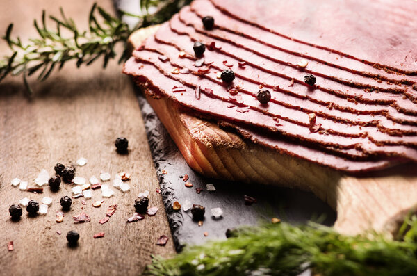 fresh sliced beef pastrami surrounded by herbs in wooden chopping board
