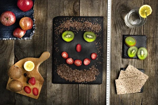 Lustiges Gesicht aus Leinsamen, Kiwi und Erdbeere auf schwarzem Stein. gesunde Ernährung, Ernährungskonzept. frische Früchte auf Holzgrund. — Stockfoto
