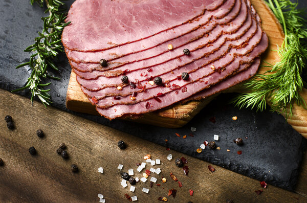 fresh sliced beef pastrami surrounded by herbs in wooden chopping board