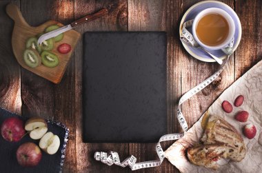 Ev yapımı panini, çay ve sağlıklı meyve ahşap arka plan üzerinde. Siyah boş taş kopya alanı ile ortada. Diyet kavramı.