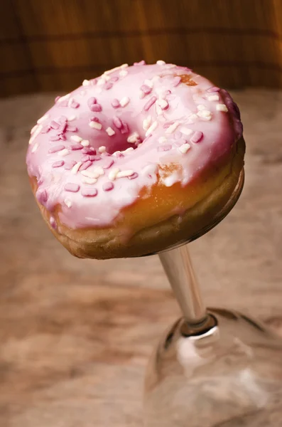 Домашний пончик, расположенный у основания стекла на деревянном фоне. Розовая глазурь на пончике . — стоковое фото