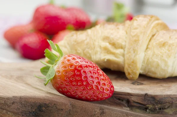 Frische Erdbeeren und frisch gebackenes Buttercroissant auf Holzuntergrund. Studioaufnahme. — Stockfoto