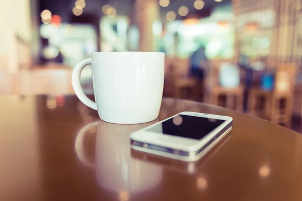 Tazza di caffè bianco in caffetteria con telefono cellulare — Foto Stock