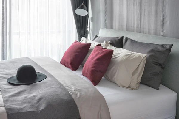 Красные подушки и черная шляпа на кровати в современной спальне — стоковое фото