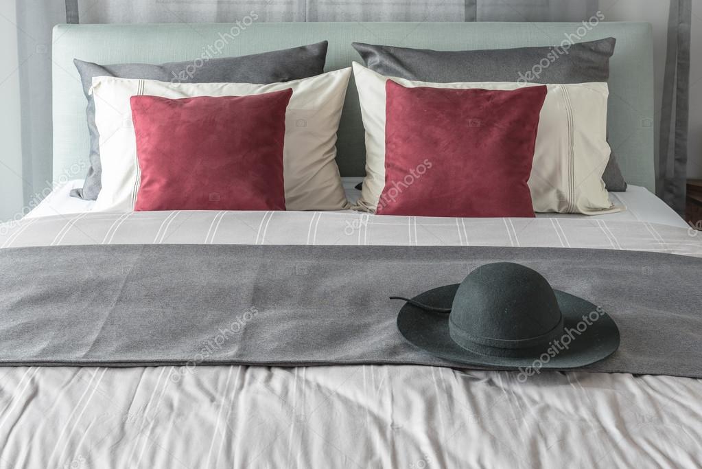Cojines rojos y sombrero negro sobre la cama en dormitorio moderno