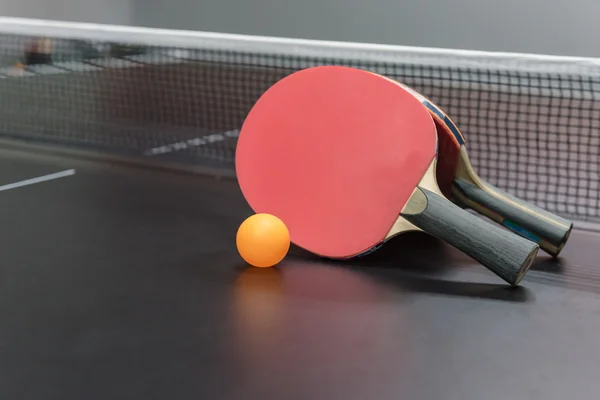 Balle orange avec raquette de ping-pong rouge sur table noire — Photo