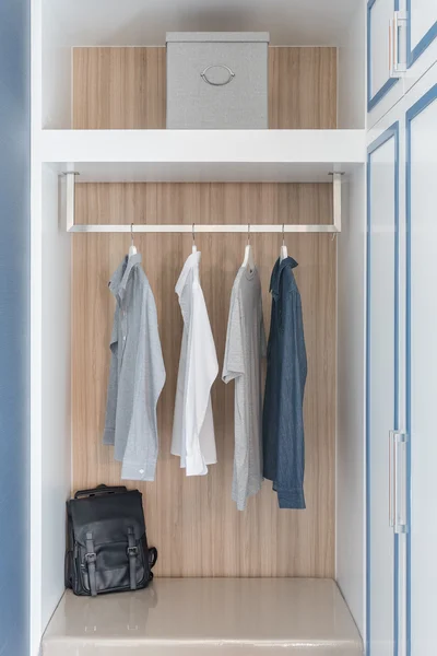 Clothes hang on rail in wooden closet — Stock Photo, Image