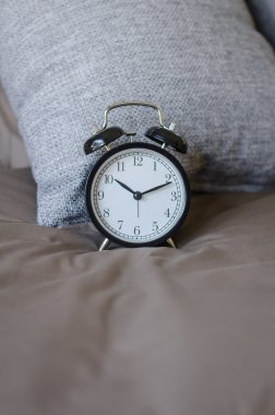 gri yastık ile kahverengi yatakta siyah çalar saat 